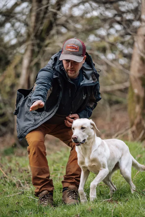 Ashley "Chalkie" White crouching beside his white Labrador in a field